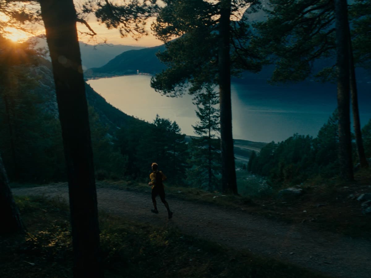 A lone trail runner on a pine-lined path high above Lake Garda at sunrise
